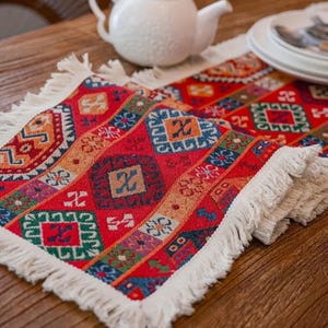 May include: A red, orange, green, blue, and yellow patterned table runner with white fringe. The runner is made of woven fabric and has a geometric design.