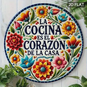 May include: A round, decorative ceramic plate with a floral design. The plate features the text "LA COCINA ES EL CORAZÓN DE LA CASA" in navy blue, surrounded by colorful flowers in red, orange, yellow, and blue. The border is navy blue.