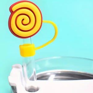 May include: A yellow and red silicone straw topper shaped like a swirl candy. The straw topper is attached to a clear drinking straw.