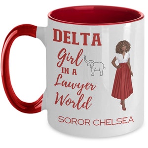 May include: White ceramic mug with a red rim and handle. The mug features a red graphic of a woman in a red skirt and a white elephant. The text on the mug reads "DELTA Girl in a Lawyer World SOROR CHELSEA".