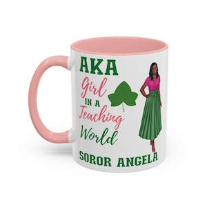 Puede incluir: Taza de cerámica blanca con borde y asa de color rosa. La taza presenta una hoja de hiedra verde, el texto "AKA Girl in a Teaching World" y el texto "Soror Angela". Una imagen de dibujos animados de una mujer con una blusa rosa y una falda verde se encuentra en el lado derecho de la taza.