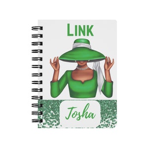 May include: A green spiral notebook with a white cover featuring a woman wearing a green hat and green dress. The text "LINK" is at the top of the cover and the name "Tosha" is at the bottom.