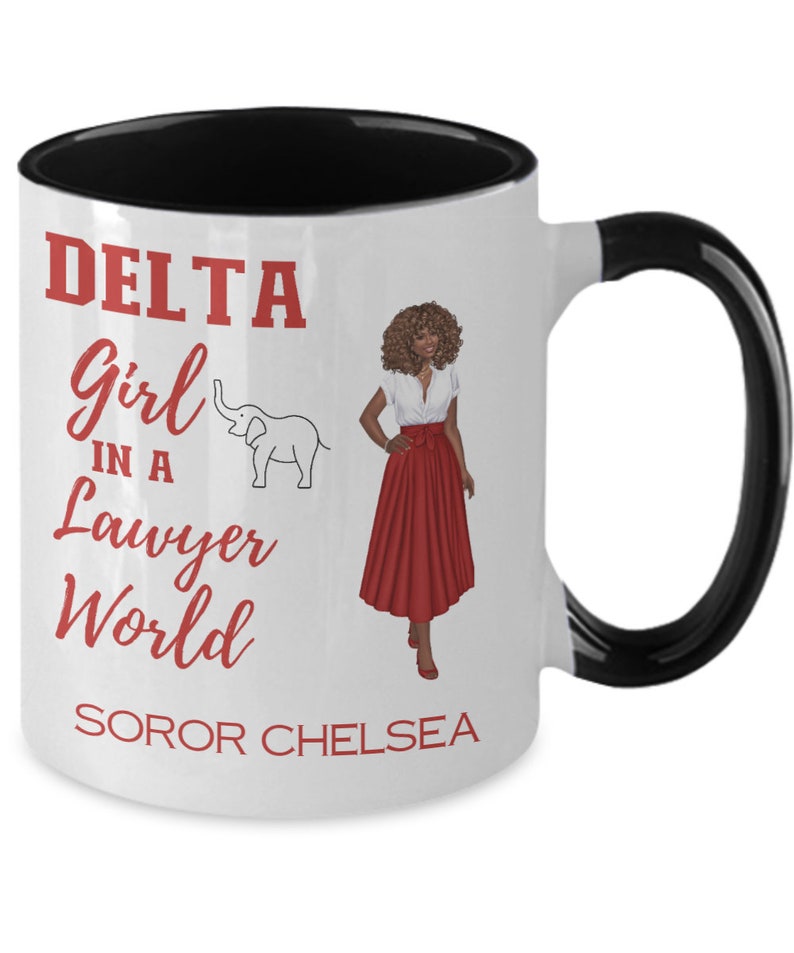 May include: White ceramic coffee mug with a black rim and handle. The mug has a red graphic that says "DELTA Girl in a Lawyer World" with a small elephant illustration. The graphic also includes the text "SOROR CHELSEA".