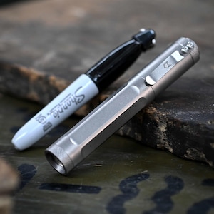 May include: A silver metal pen with a pocket clip and a black Sharpie marker. The pen has a hexagonal body and a small logo near the clip. The Sharpie is white with black ink and the Sharpie logo.