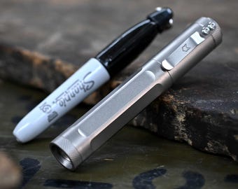 May include: A silver metal pen with a pocket clip and a black Sharpie marker. The pen has a hexagonal body and a small logo near the clip. The Sharpie is white with black ink and the Sharpie logo.