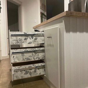 Puede incluir: Armarios de cocina blancos con tres cajones que tienen un forro de papel tapiz con estampado floral. Los cajones est&aacute;n abiertos y el armario est&aacute; en una cocina.