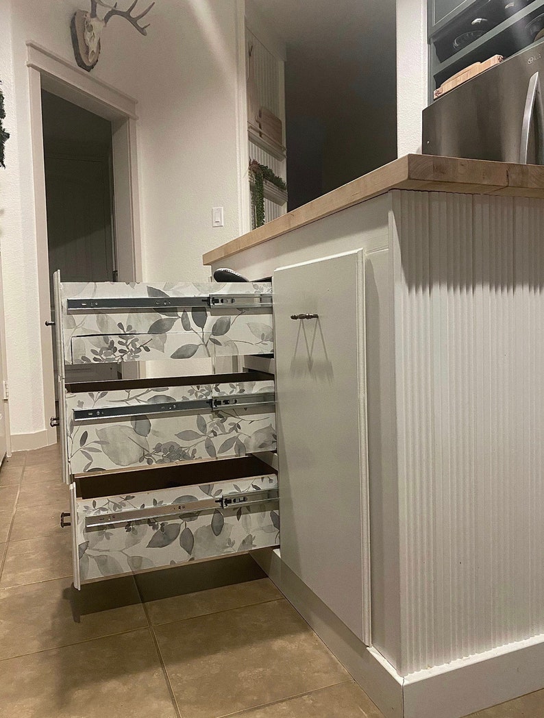 Puede incluir: Armarios de cocina blancos con tres cajones que tienen un forro de papel tapiz con estampado floral. Los cajones est&aacute;n abiertos y el armario est&aacute; en una cocina.