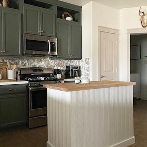 Puede incluir: Una isla de cocina con una encimera de madera y una base de metal corrugado blanco. La isla est&aacute; frente a una cocina verde con electrodom&eacute;sticos de acero inoxidable.