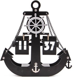 Può includere: Orologio nero a forma di ancora con timone argentato e dettagli a catena. L'orologio segna le 11:37. Una piccola ancora argentata è in basso al centro. Un oggetto decorativo a tema nautico.
