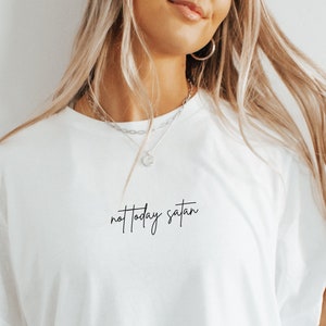 Puede incluir: Camiseta blanca con el texto "not today satan" en letra negra.