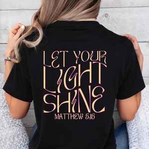 May include: Black t-shirt with the text "Let your light shine" in pink and gold lettering. The text "Matthew 5:16" is printed below the main text.