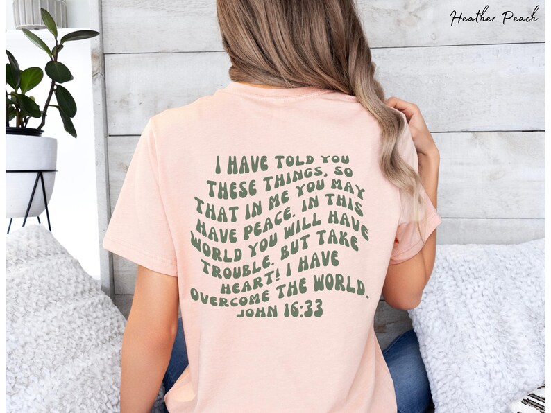 May include: A pink t-shirt with a green text graphic that reads "I have told you these things, so that in me you may have peace. In this world you will have trouble. But take heart! I have overcome the world. John 16:33"