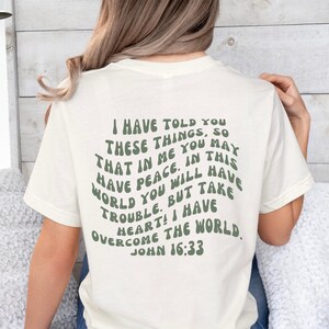 May include: A white t-shirt with a green text graphic that reads "I have told you these things, so that in me you may have peace. In this world you will have trouble. But take heart! I have overcome the world. John 16:33"