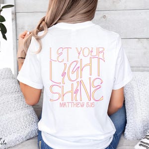 May include: White t-shirt with the text "Let your light shine" in pink and yellow lettering. The text "Matthew 5:16" is printed below the main text.