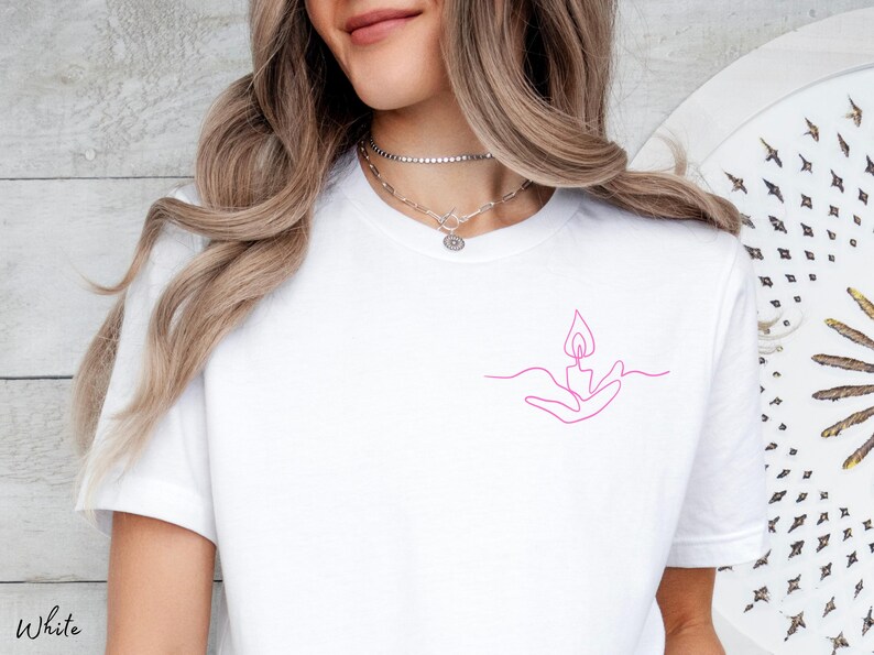 May include: White t-shirt with a pink line drawing of a hand holding a flame.