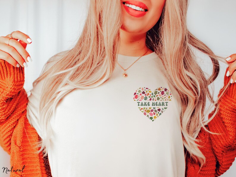 May include: White t-shirt with a floral heart design and the text "Take Heart" in green letters.