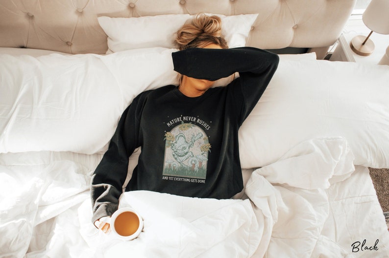 May include: A black sweatshirt with a graphic print of a creature with the text "Nature never rushes and yet everything gets done".