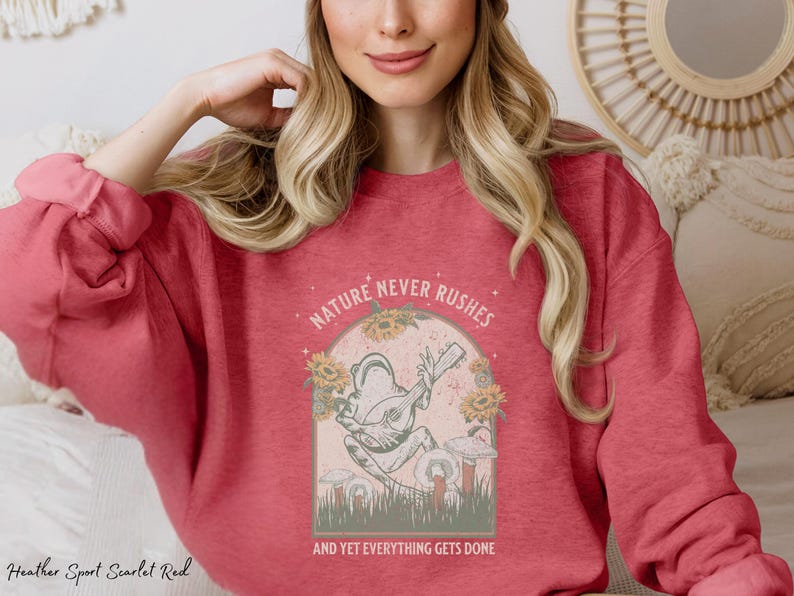 May include: A heather sport scarlet red sweatshirt with a graphic of a frog playing a guitar. The graphic is surrounded by flowers and the text "Nature never rushes and yet everything gets done".