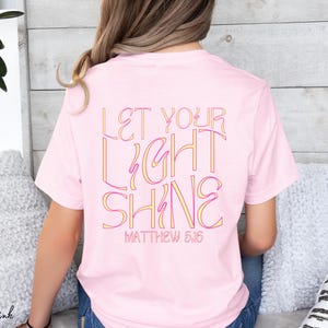 May include: A pink t-shirt with the text "Let Your Light Shine" and "Matthew 5:16" in a colorful, outlined font.