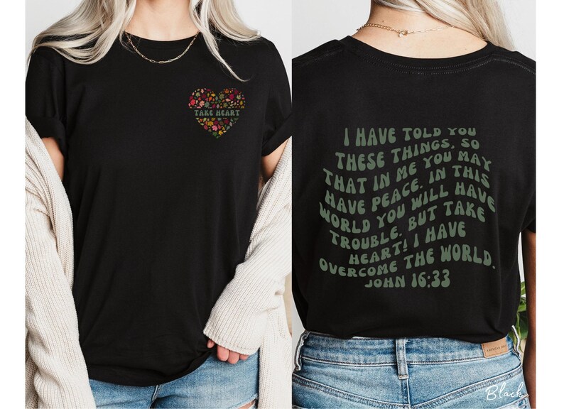 May include: Black t-shirt with a floral heart design on the front and a green text quote on the back that reads "I have told you these things, so that in me you may have peace. In this world you will have trouble. But take heart! I have overcome the world. John 16:33"