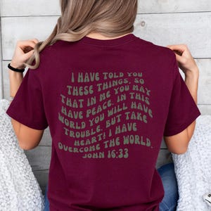 May include: Maroon t-shirt with a white text graphic that reads "I have told you these things, so that in me you may have peace. In this world you will have trouble. But take heart! I have overcome the world. John 16:33"