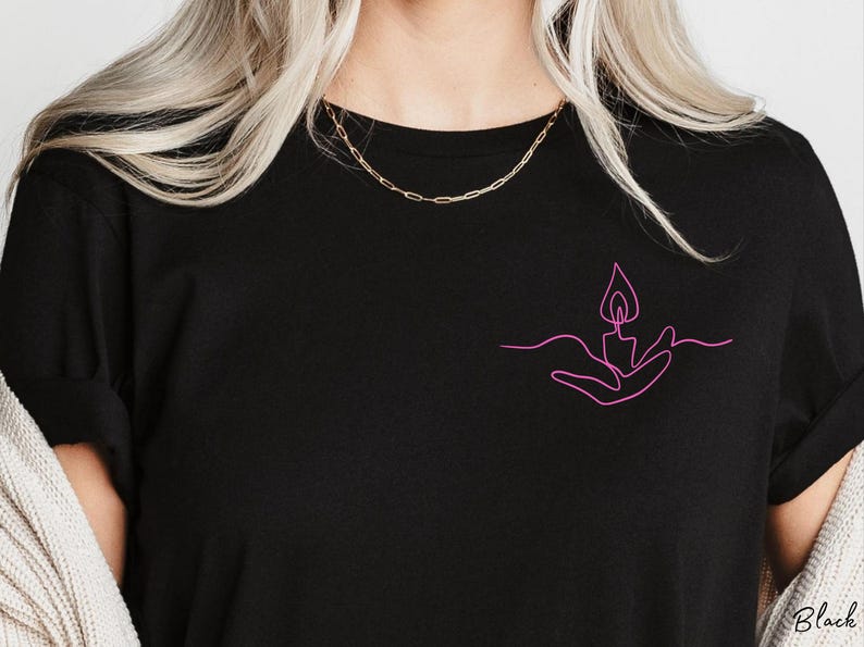 May include: A black t-shirt with a pink line drawing of a hand holding a candle flame.