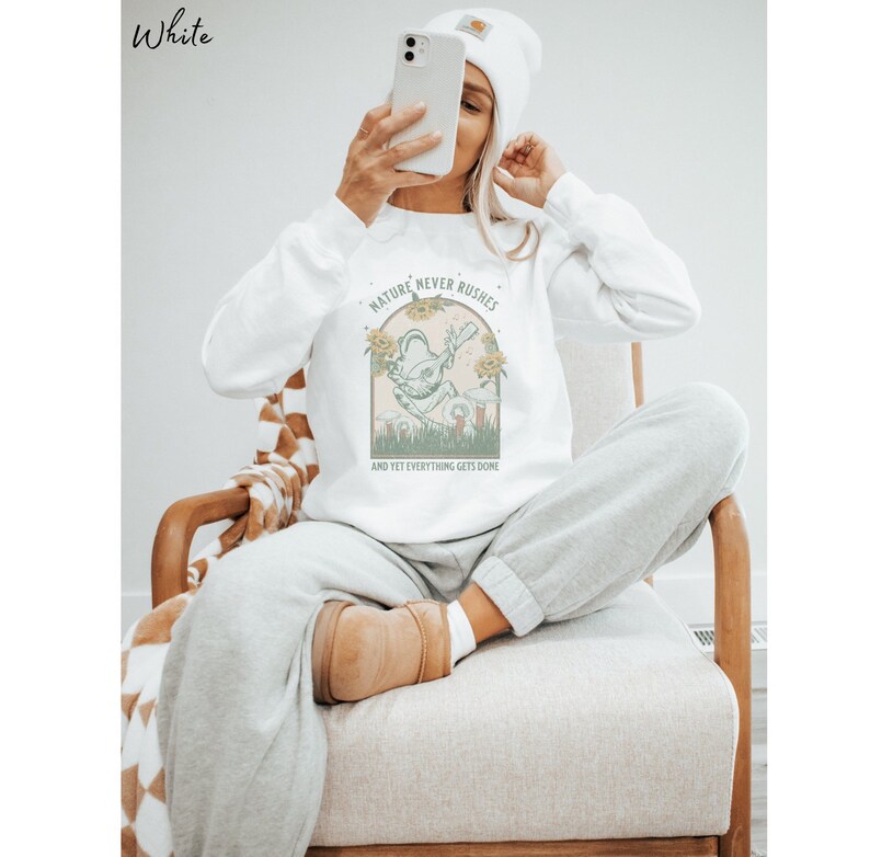 May include: White sweatshirt with a green frog graphic and the text "Nature never rushes and yet everything gets done".