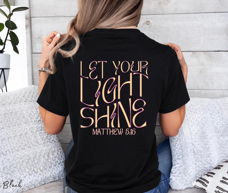 May include: Black t-shirt with the text "Let your light shine" in pink and gold lettering. The text "Matthew 5:16" is printed below the main text.