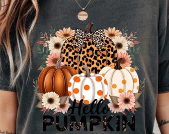 May include: Dark gray t-shirt featuring a fall-themed design. The design includes three pumpkins, sunflowers, and the text "Hello Pumpkin." One pumpkin has a leopard print pattern. The other two pumpkins have orange polka dots.