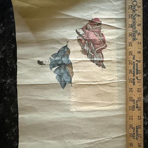 May include: A light beige paper sheet featuring two illustrated figures in traditional attire, one in blue and one in red, positioned next to a wooden ruler measuring 35 inches in length, with text reading Clyde Savings Bank.