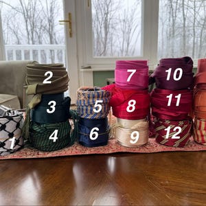May include: An assortment of colorful fabric rolls and decorative baskets. The rolls are in various colors, including green, blue, pink, red, and orange. The baskets are black and white with a geometric pattern. The items are arranged on a table.
