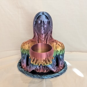May include: A rainbow-colored resin sculpture of a woman holding a copper singing bowl. The sculpture is detailed with intricate patterns and textures.