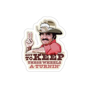 Può includere: Un'illustrazione di un uomo con un cappello da cowboy e una camicia rossa, che fa il segno della pace. Il testo dice "Got to Keep These Wheels A-Turnin'"