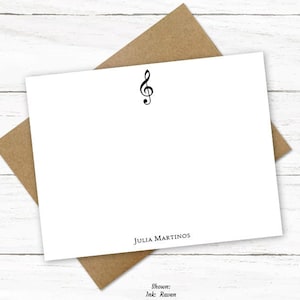 May include: White stationery card with a treble clef symbol and the name "JULIA MARTINOS" printed in black at the bottom. The card is on a brown paper envelope.