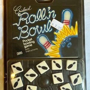 May include: A black and yellow game box with the text "Roll'n Bowl" and "Pocket bowling game with instructions". The box contains 10 white dice with black bowling pins printed on them. The price tag reads "$2.95".