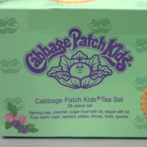 May include: A mint green Cabbage Patch Kids tea set box. The box features the Cabbage Patch Kids logo in purple, along with images of cookies and a heart-shaped pastry. Text on the box reads "Cabbage Patch Kids Tea Set 28-piece set."