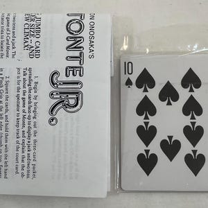 May include: A playing card from a deck, featuring the number 10 and ten black spade symbols. The card is in a clear plastic sleeve next to a white paper with black text that reads "TONTE JR."