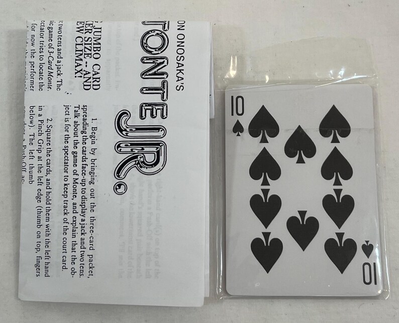 May include: A playing card from a deck, featuring the number 10 and ten black spade symbols. The card is in a clear plastic sleeve next to a white paper with black text that reads "TONTE JR."