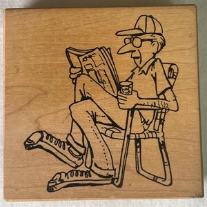 May include: A black and white line drawing of a person sitting in a chair, reading a newspaper and holding a glass. The person is wearing a hat and glasses.
