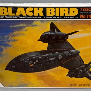 May include: A model kit box for the Lockheed SR-71 Blackbird, a strategic air command reconnaissance aircraft. The box features a black aircraft illustration against a yellow and orange background. Text includes "BLACK BIRD" and "1:72 scale".