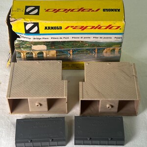 May include: A set of two brown plastic bridge piers for a model train set. The piers are labeled "Arnold rapido" and are made in Germany. The set also includes two black plastic bases.