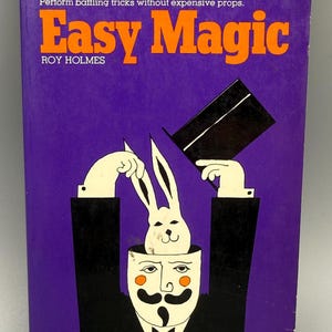 May include: A vintage book cover for "Easy Magic" by Roy Holmes. The cover is purple with orange text and a graphic of a magician with a rabbit in their head. The magician is wearing a black suit and a white mask.