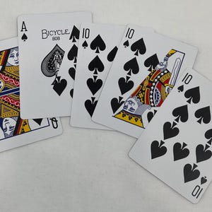 May include: A spread of playing cards featuring the Queen of Spades, Ace of Spades, and several 10 of Spades cards. The Bicycle brand is visible on the Ace of Spades. The cards are white with black spade symbols and colorful court card designs.