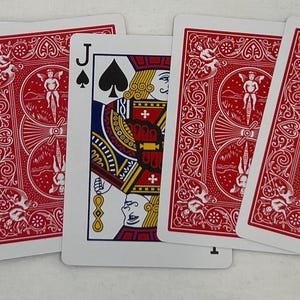 May include: A collection of playing cards featuring a Jack of Spades card in the center, flanked by four cards with red backs. The Jack of Spades card displays a detailed illustration with black, gold, red, and blue colors. The backs of the cards have a red ornate design.