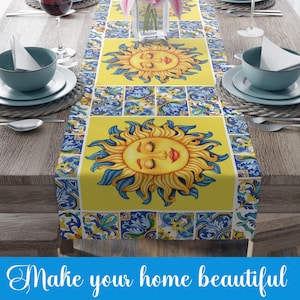 May include: Yellow table runner with a blue and white tile pattern and a repeating image of a smiling sun with closed eyes. The table runner is on a wooden table.