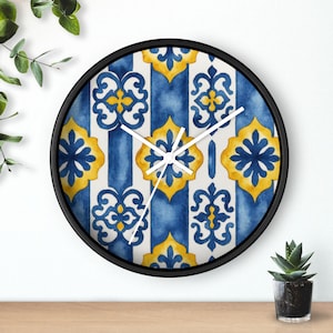 May include: A round wall clock with a black frame. The clock face features a blue and yellow floral pattern with white vertical stripes. The clock hands are white.