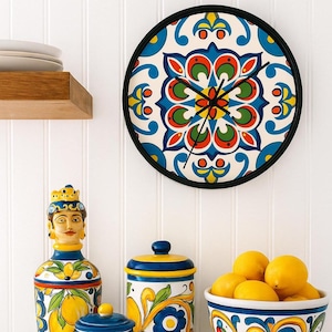 May include: A circular wall clock with a black surround and a vibrant floral pattern in blue, green, orange, and yellow. The clock hands are black. The clock is mounted on a white wall. Decorative jars and a bowl of lemons are in the foreground.