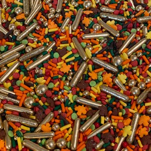 Puede incluir: Una colorida mezcla de chispas, que incluye varillas metálicas doradas, pequeñas esferas doradas y varias formas en naranja, amarillo, verde y marrón. Las chispas incluyen formas de hojas y pequeñas varillas, ideales para decorar postres.