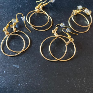 May include: Three pairs of gold hoop earrings with a simple design. The earrings are made of thin wire and have a smooth finish.