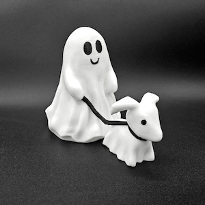 May include: A white ghost figurine with a smiling face and black eyes, holding a leash attached to a white ghost dog figurine.